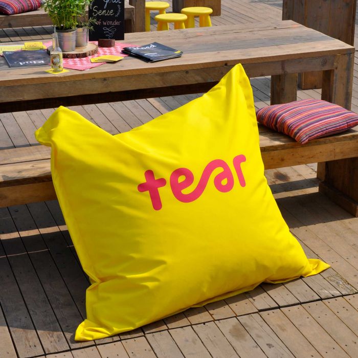 Gelber Sitzsack mit pinkem Schriftzug 'tear', platziert auf einer Holzterrasse.