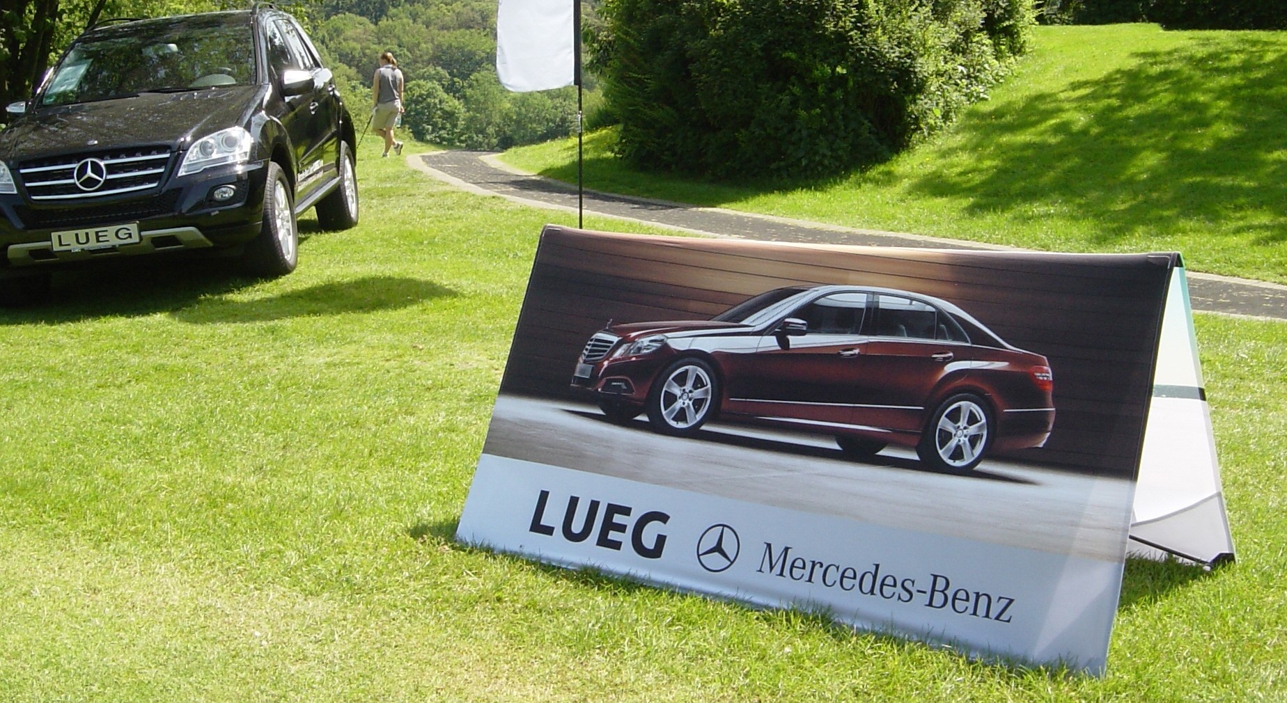 Werbebande für Mercedes-Benz mit dem Schriftzug 'LUEG' und einem Bild eines Mercedes-Fahrzeugs.
