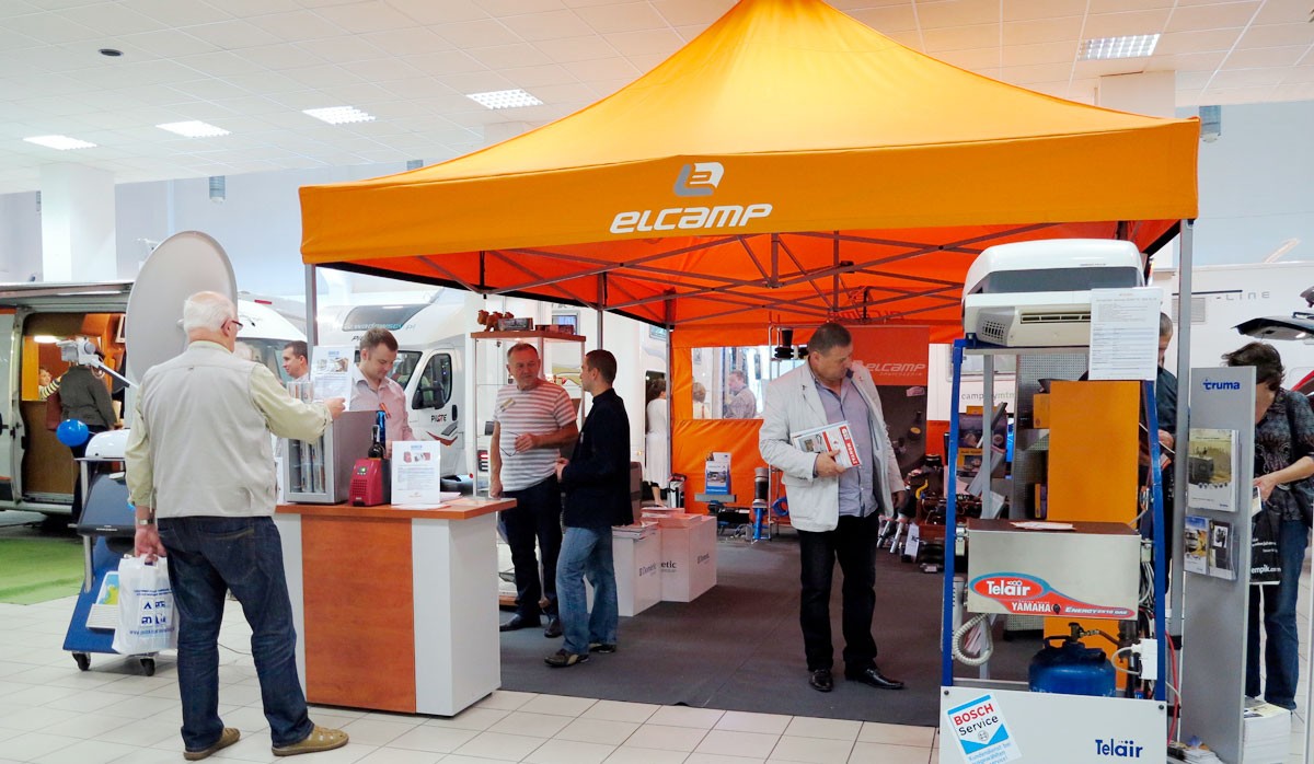 Faltzelt 3x3m Messestand von elcamp mit orangefarbenem Dach, Besucher am Stand, Produkte ausgestellt.