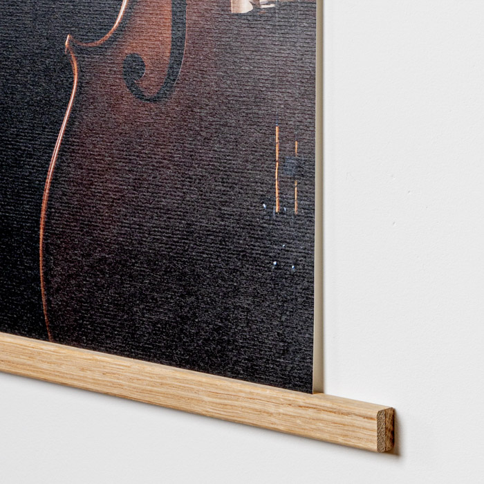 Detailaufnahme einer Posterleiste aus Holz, die ein Plakat hält, mit einem dunklen Hintergrund und einem Teil eines Instruments sichtbar.