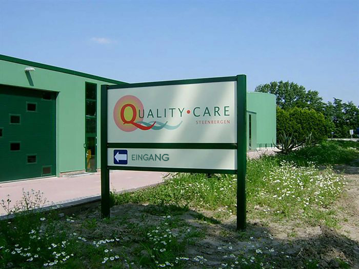 Schild mit der Aufschrift 'Quality Care Steinbergen' und dem Hinweis 'Eingang' in Richtung links.