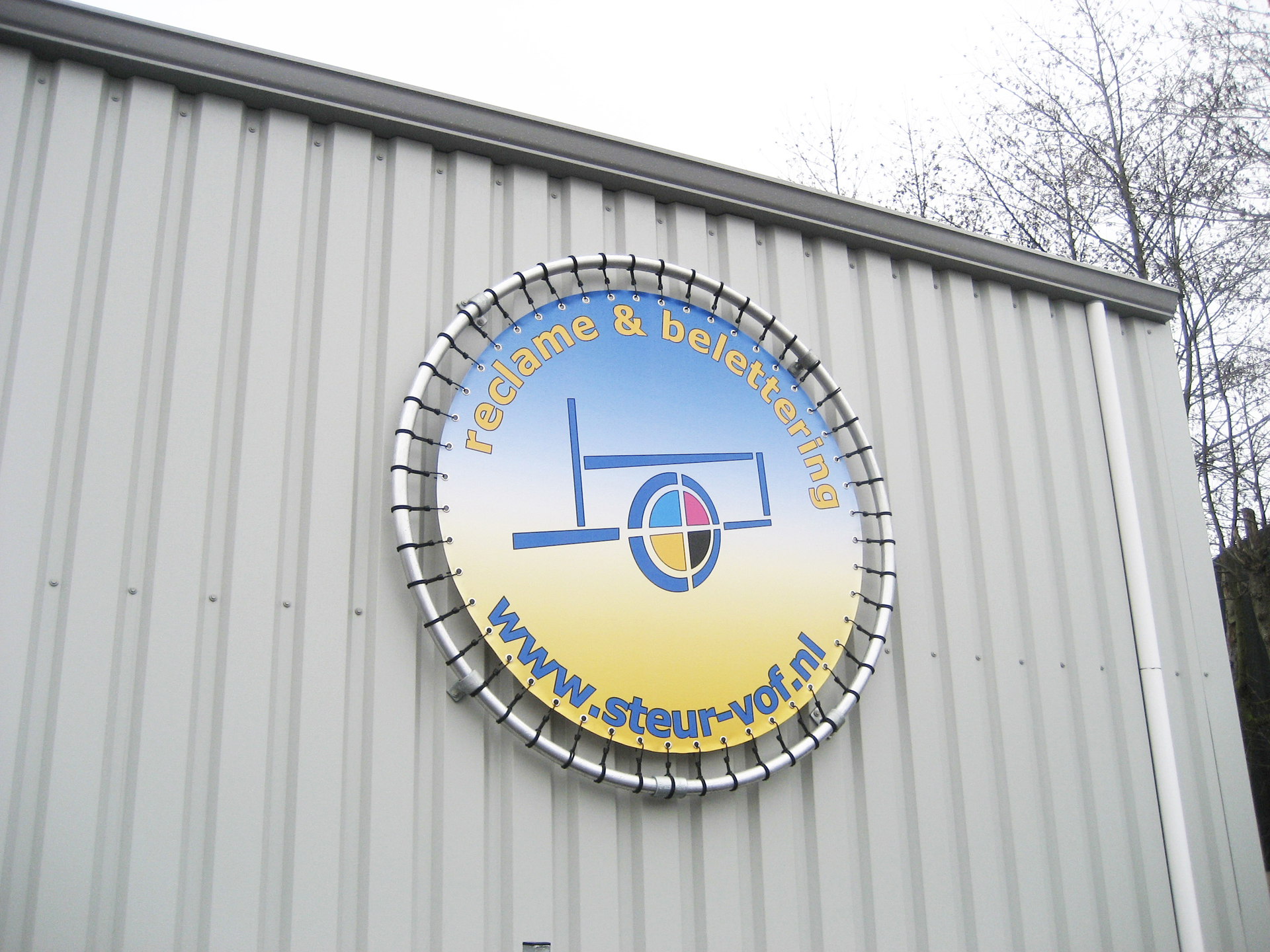 Runder Bannerrahmen für den Außenbereich mit einem bunten Design und der Aufschrift reklame & belettering sowie der Website www.steur-vor.nl.