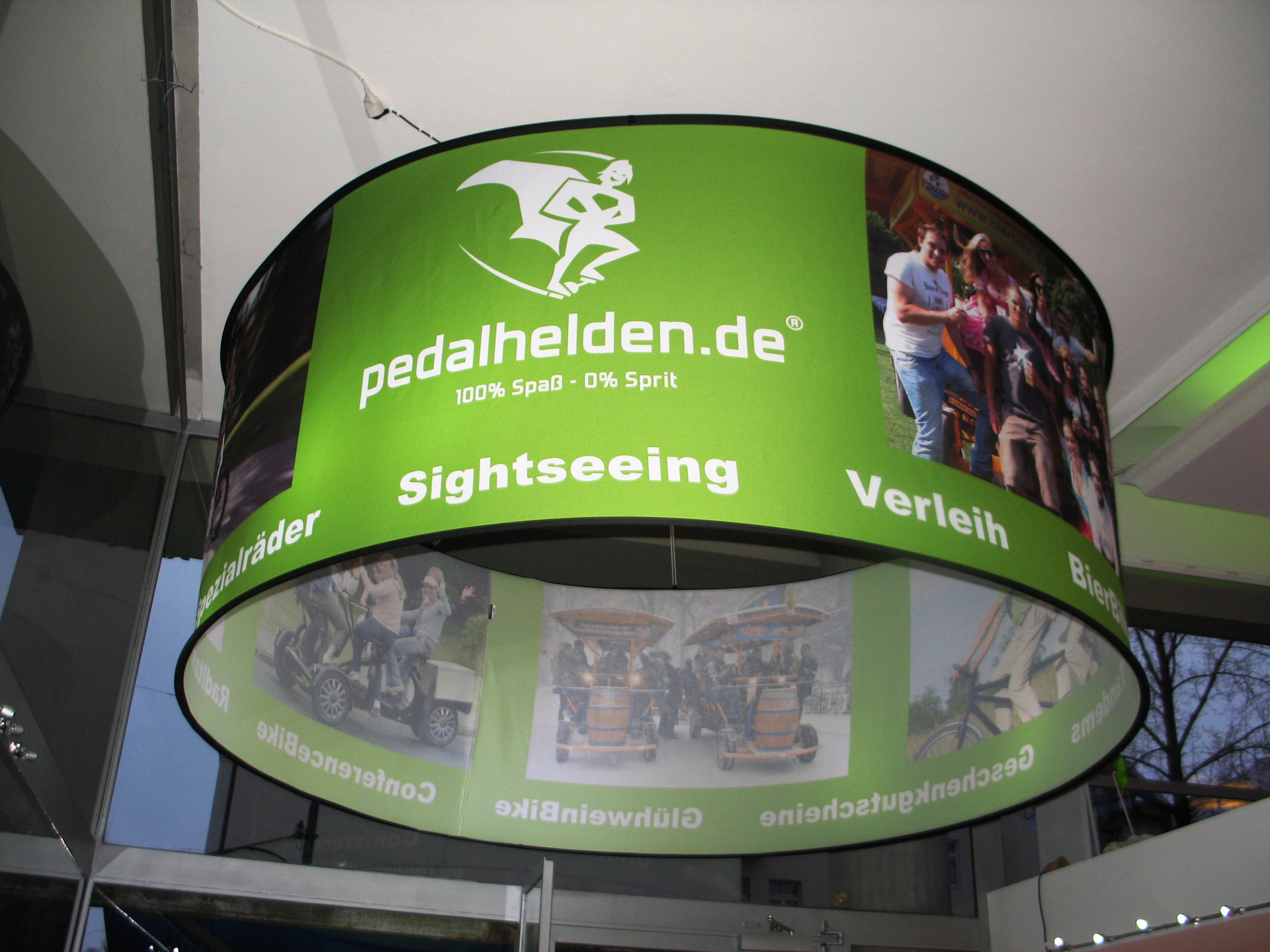Drei runde Deckenhänger mit dem Schriftzug Hertz hängen über einem Messestand. Im Hintergrund ist der Stand von Europcar sichtbar.