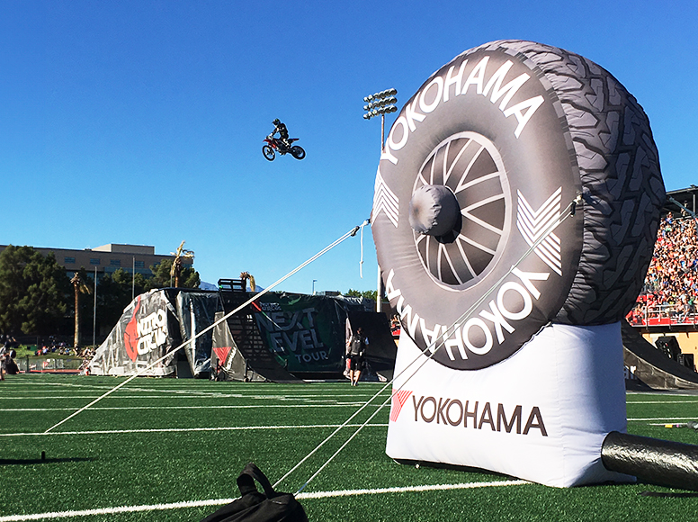 Aufblasbare Werbung in Form eines Yokohama-Reifens auf einem Sportfeld, während ein Motorradfahrer in der Luft springt.