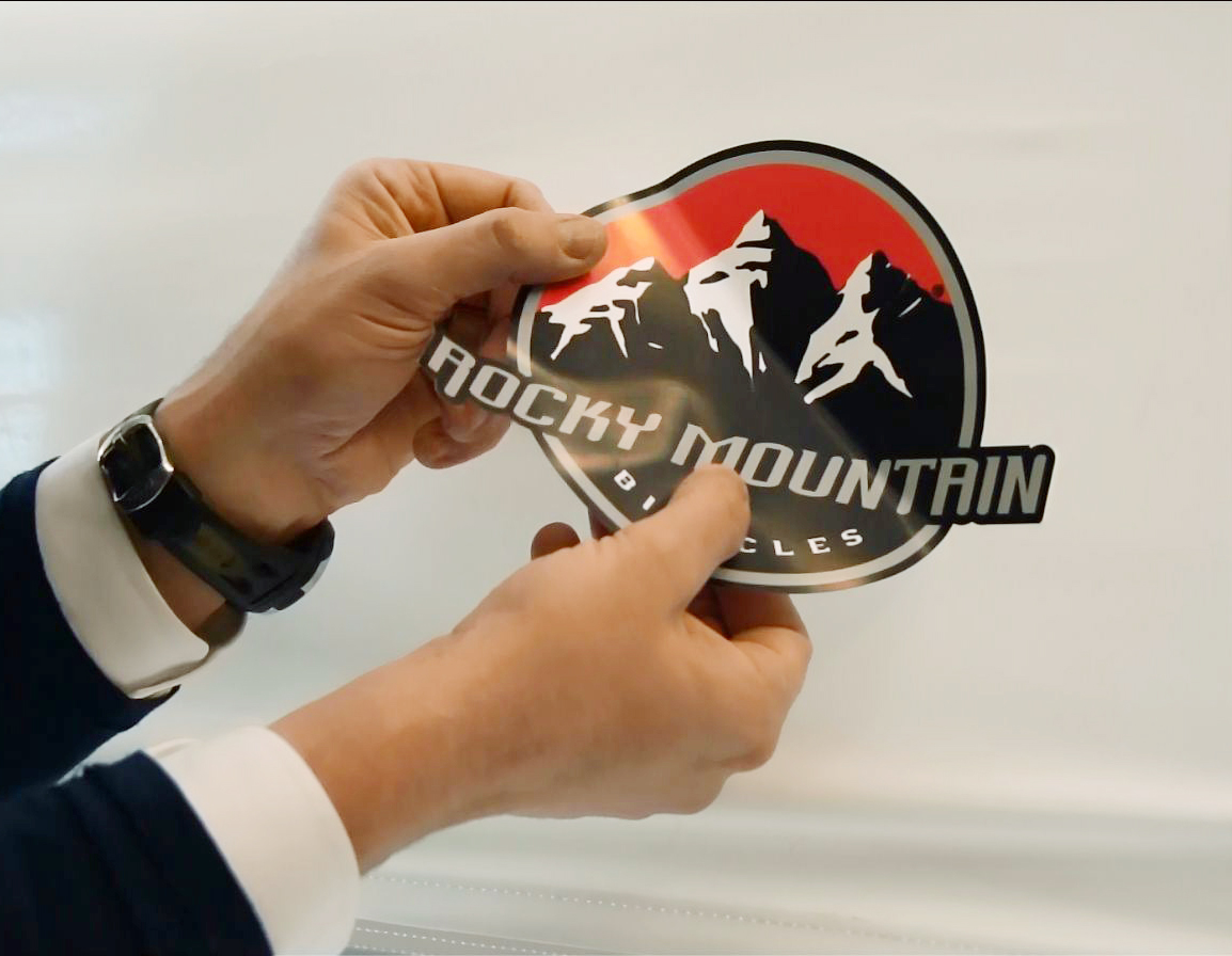 Eine Person hält eine Vinylfolie mit dem Logo Rocky Mountain Bicycles, das Berge darstellt.