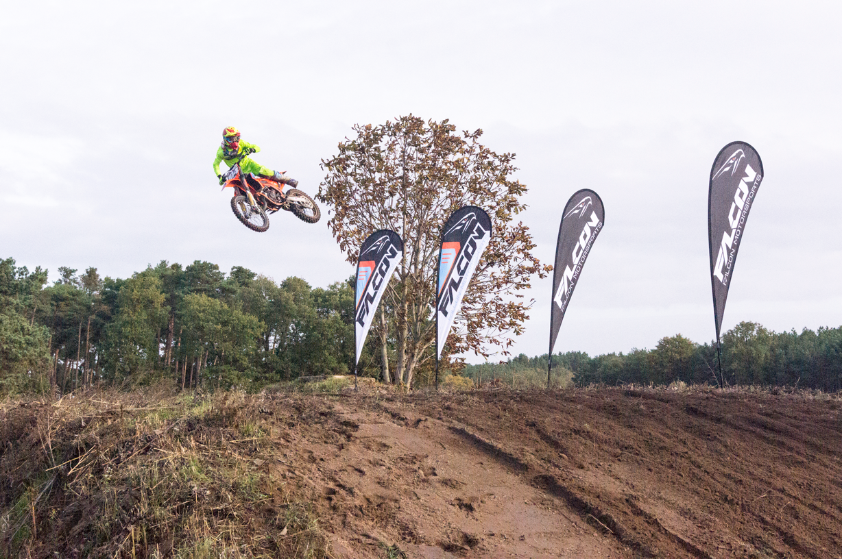 Motorradfahrer springt mit einem Dirtbike über einen Hügel, umgeben von Falcon-Flaggen.