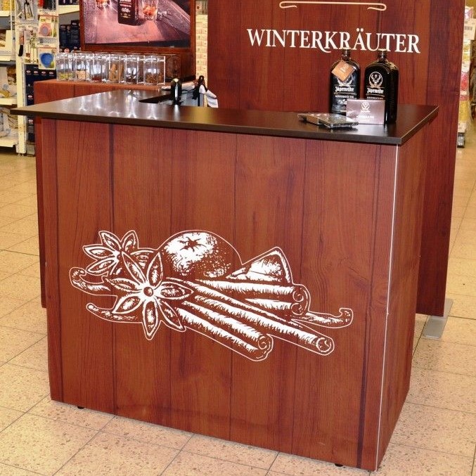 Messetheke von Jägermeister mit Holzoptik und schwarzer Arbeitsfläche, dekoriert mit einer Illustration von Gewürzen.
