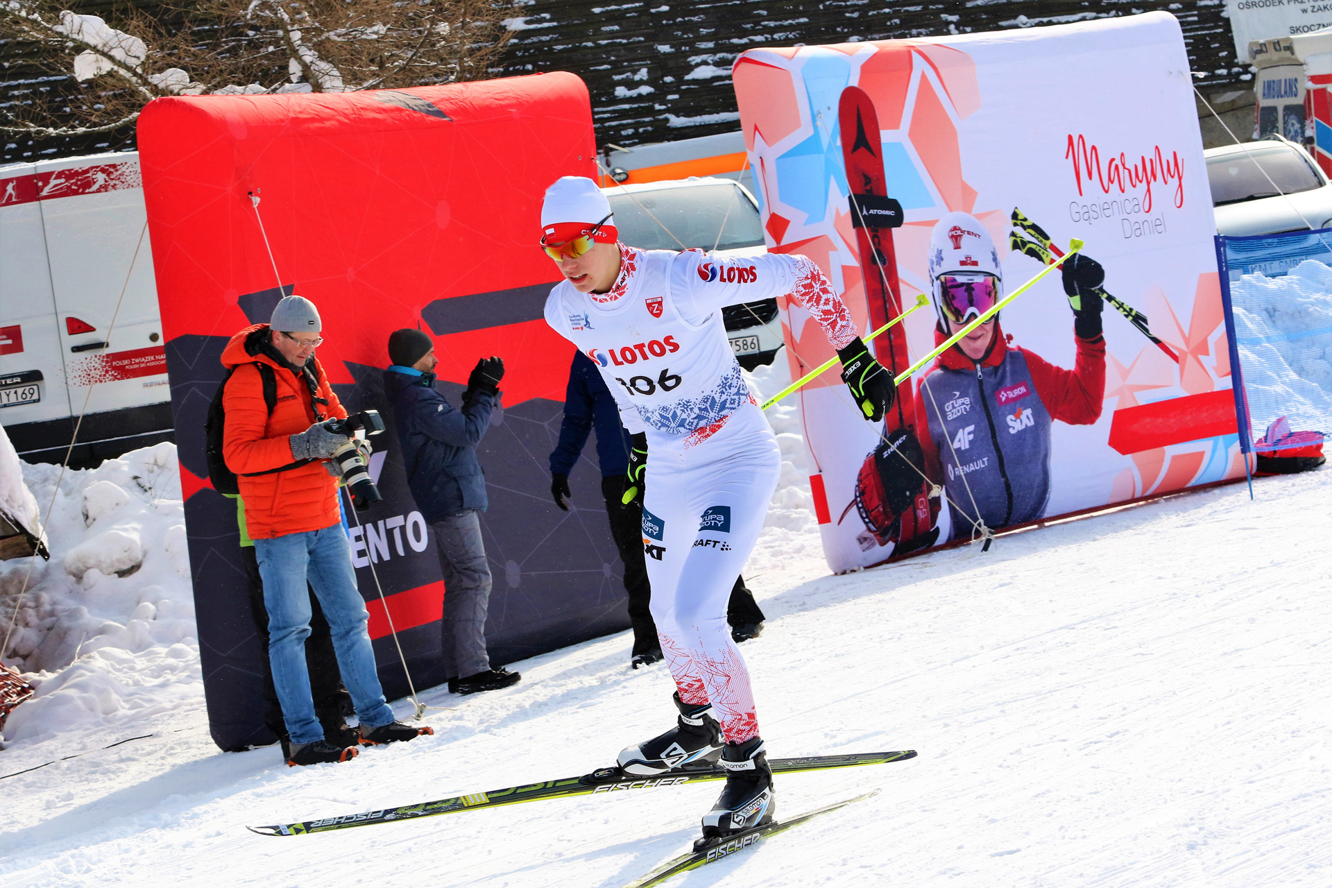 Drei Sportler stehen auf dem Siegerpodest bei einem Wintersport-Event in Begpiastow, umgeben von Schnee und Bäumen.