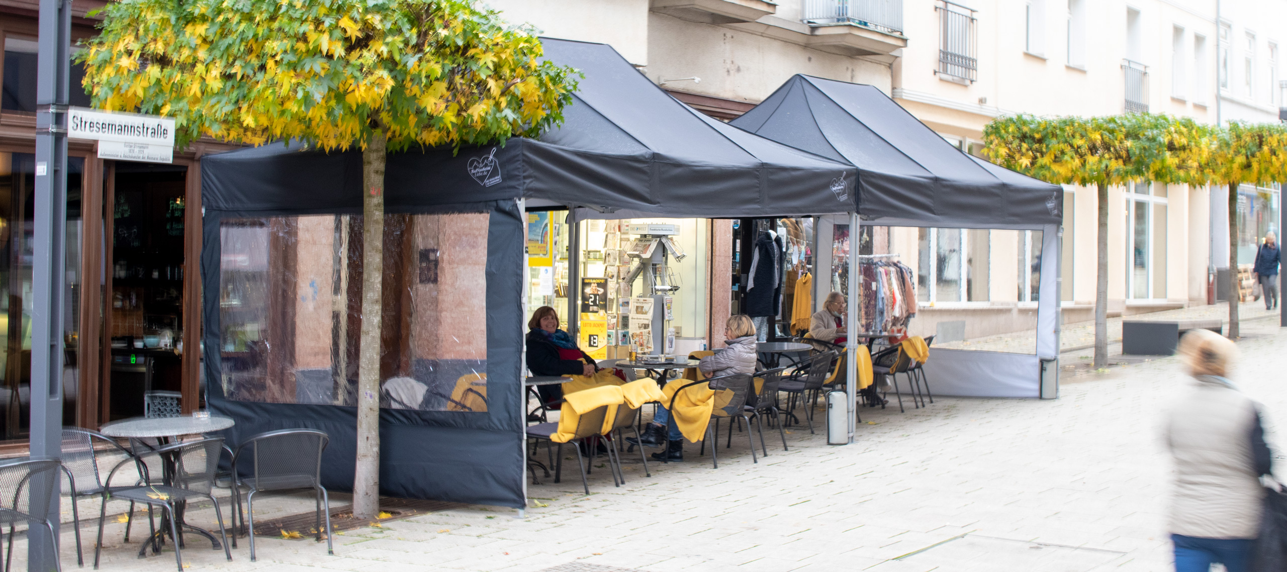 Zwei schwarze Zelte für die Außengastronomie in Bad Nauheim, mit Tischen und Stühlen, umgeben von Bäumen mit gelben Blättern.