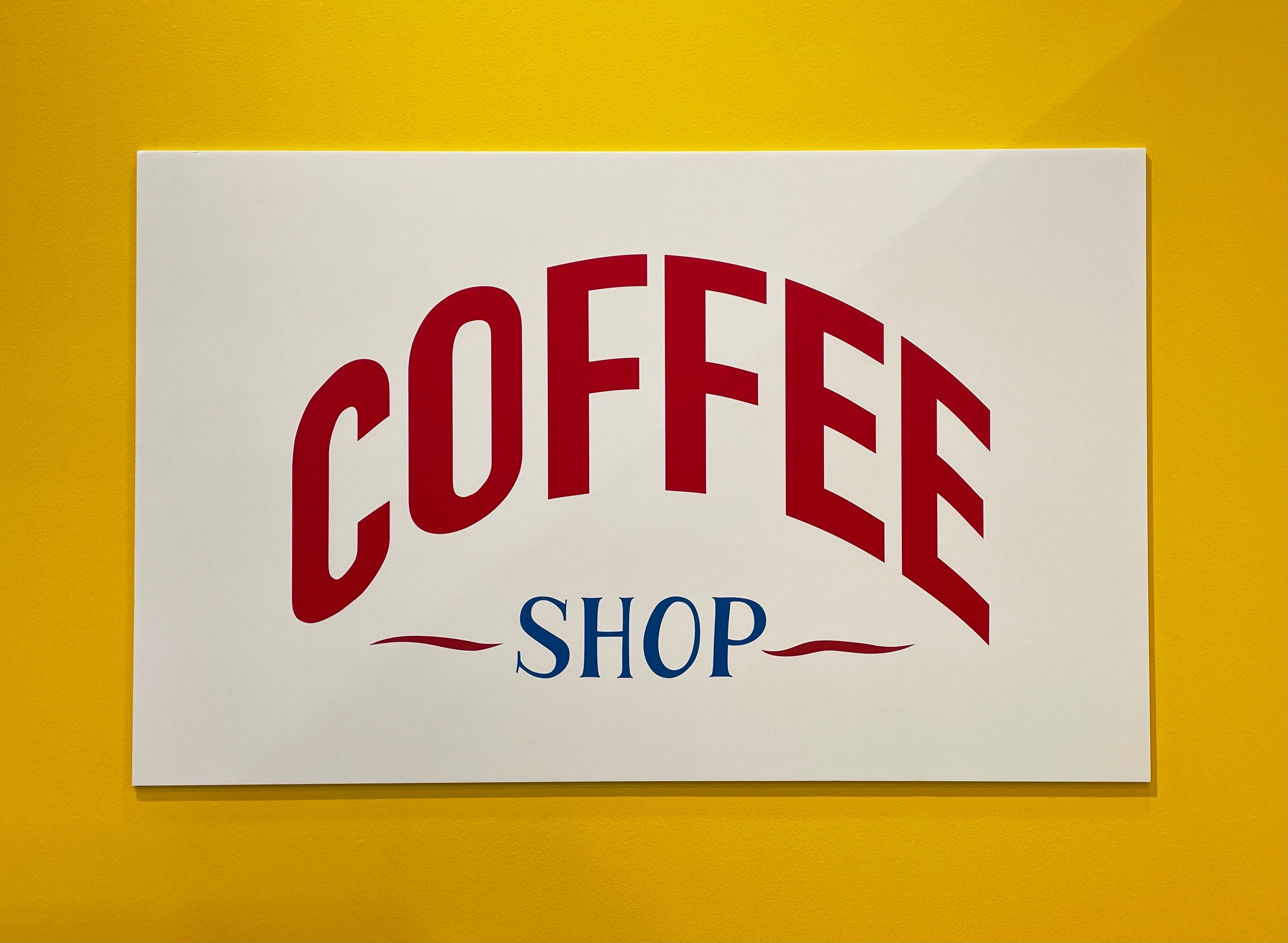 Werbeschild mit der Aufschrift 'COFFEE SHOP' in roten und blauen Buchstaben auf gelbem Hintergrund.