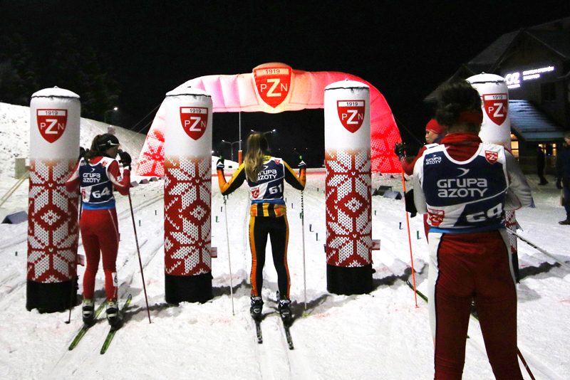 Skilangläufer stehen an der Vento Säule Pzn Blow Up, umgeben von Schnee und beleuchtet von Nachtlichtern.
