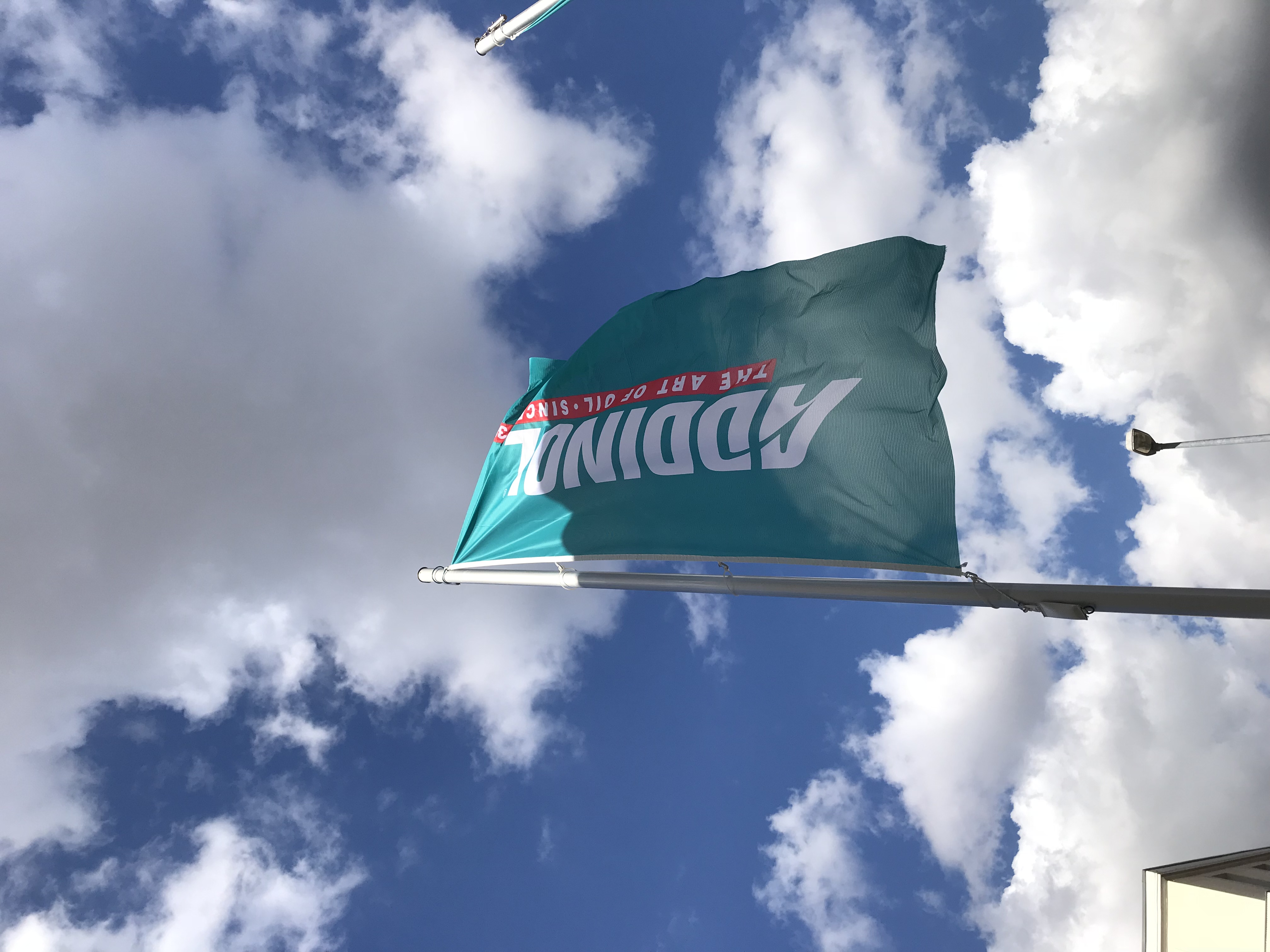 Flagge von ADDINOL mit dem Slogan 'Take Part. Be Active.' vor einem wolkigen Himmel.