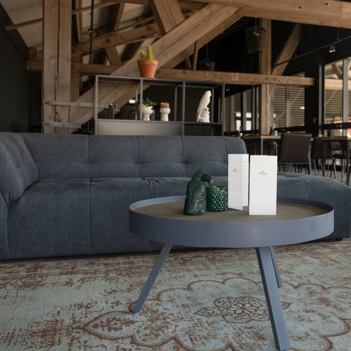 Sitzecke Gastronomie mit grauem Sofa und runder Tisch mit zwei weißen Karten auf einem Teppich.