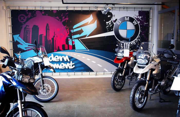 Banner mit BMW-Logo und urbanem Design, Motorräder im Vordergrund.