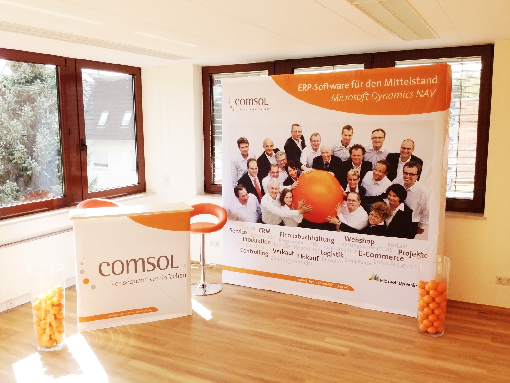 Messewand mit dem Produktnamen Messewand Quickup Stoffwand Medium Front und Seiten von Comsol, zeigt Team mit orangefarbener Kugel, Werbung für ERP-Software.