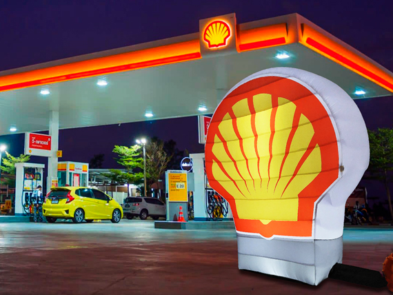 Shell Logo an einer Tankstelle mit beleuchtetem Logo und gelbem Auto im Hintergrund.