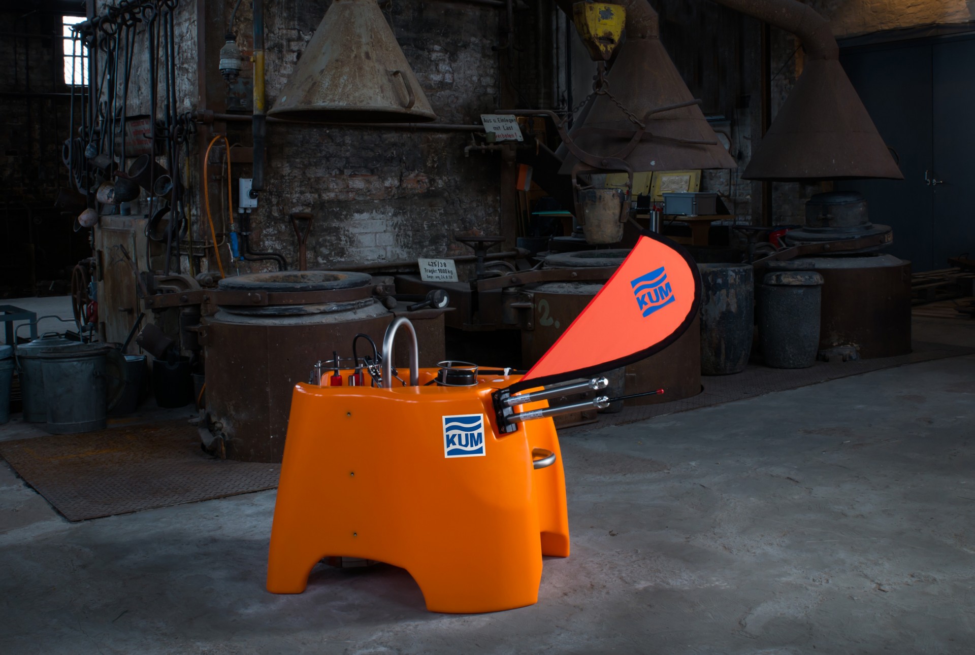 Tischaufstelle Easyflag Micro von KUM in leuchtendem Orange, mit einem auffälligen roten Flaggenelement, in einer industriellen Umgebung.