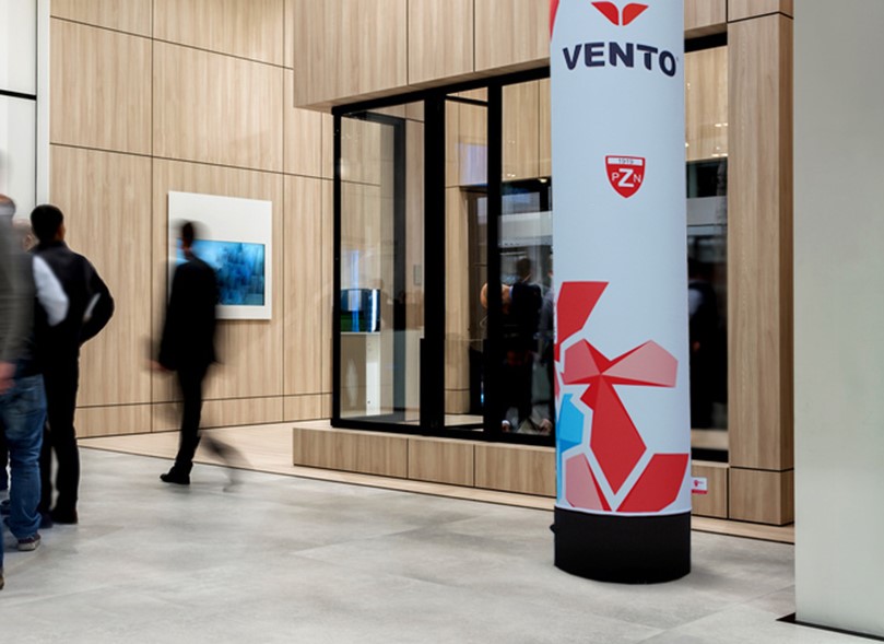 Vento Säule Innen in einem modernen Innenraum mit Holzverkleidung und Menschen im Hintergrund.
