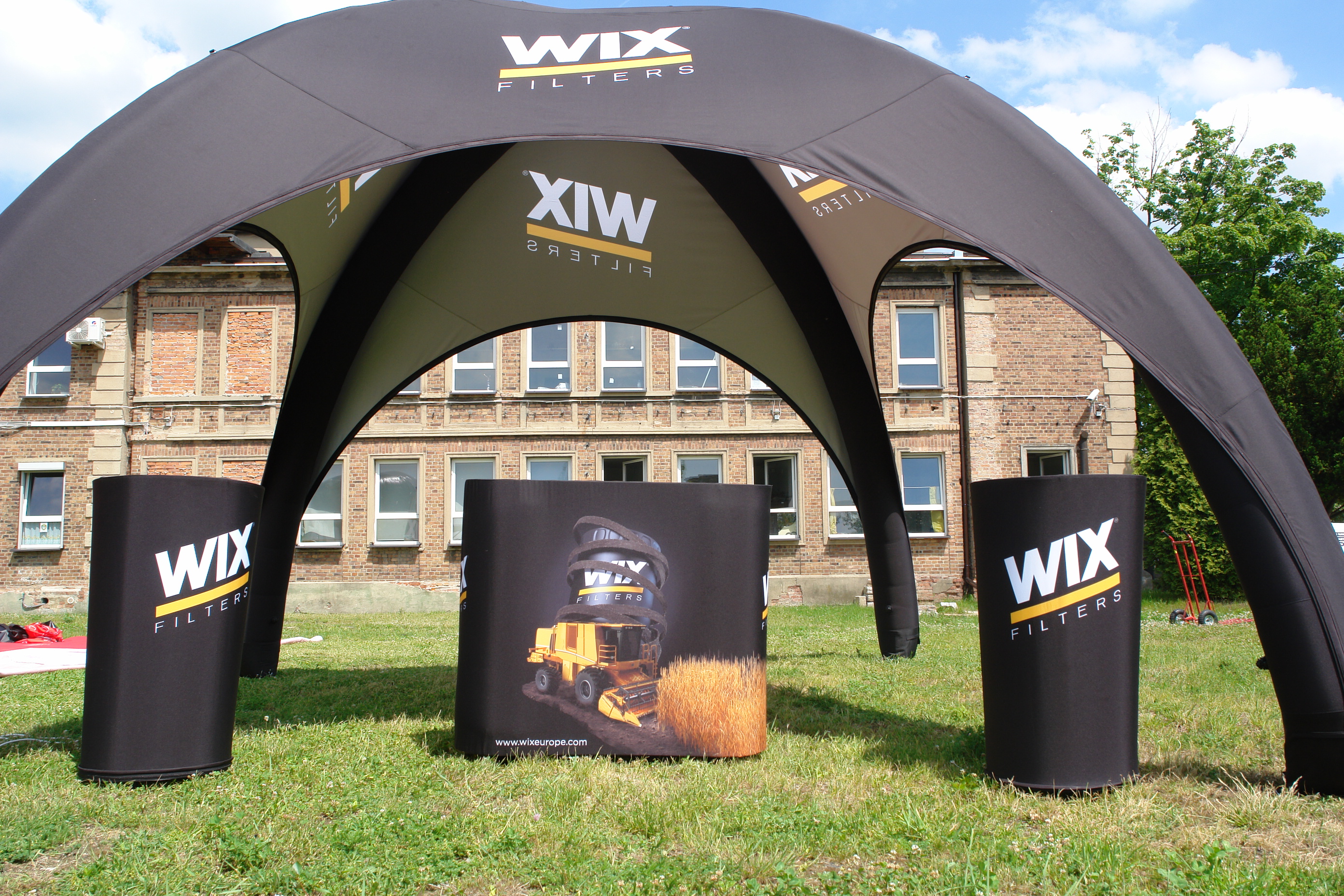 Vento Zelt mit Theke von ENTDECKER, schwarz mit WIX FILTERS Logo, auf einer Wiese vor einem Gebäude.