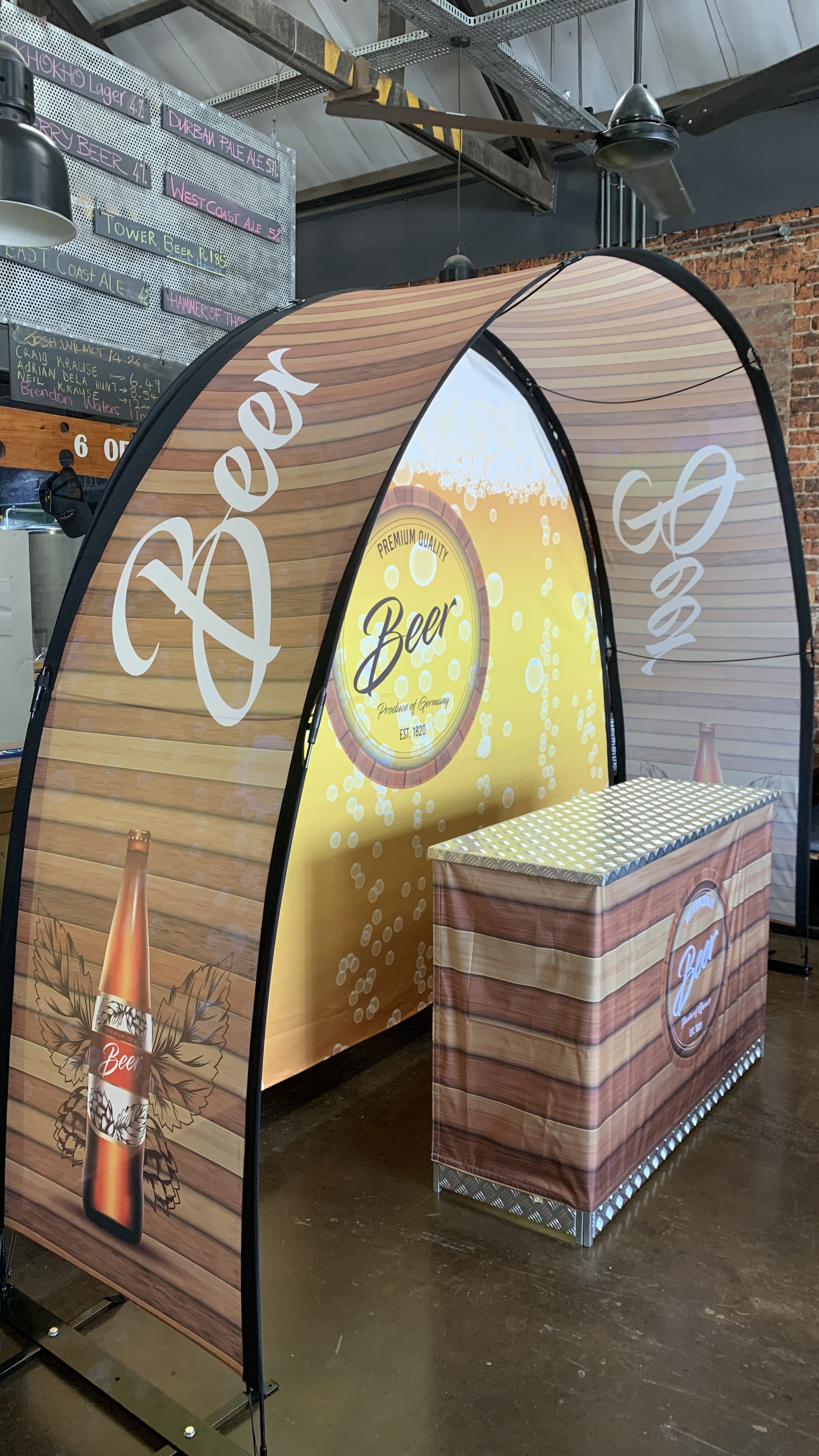 Eventbogen Displaybow Messe von ENTDECKER mit blauem Hintergrund und Logo, zeigt einen Stand mit einem Tisch und zwei Personen.