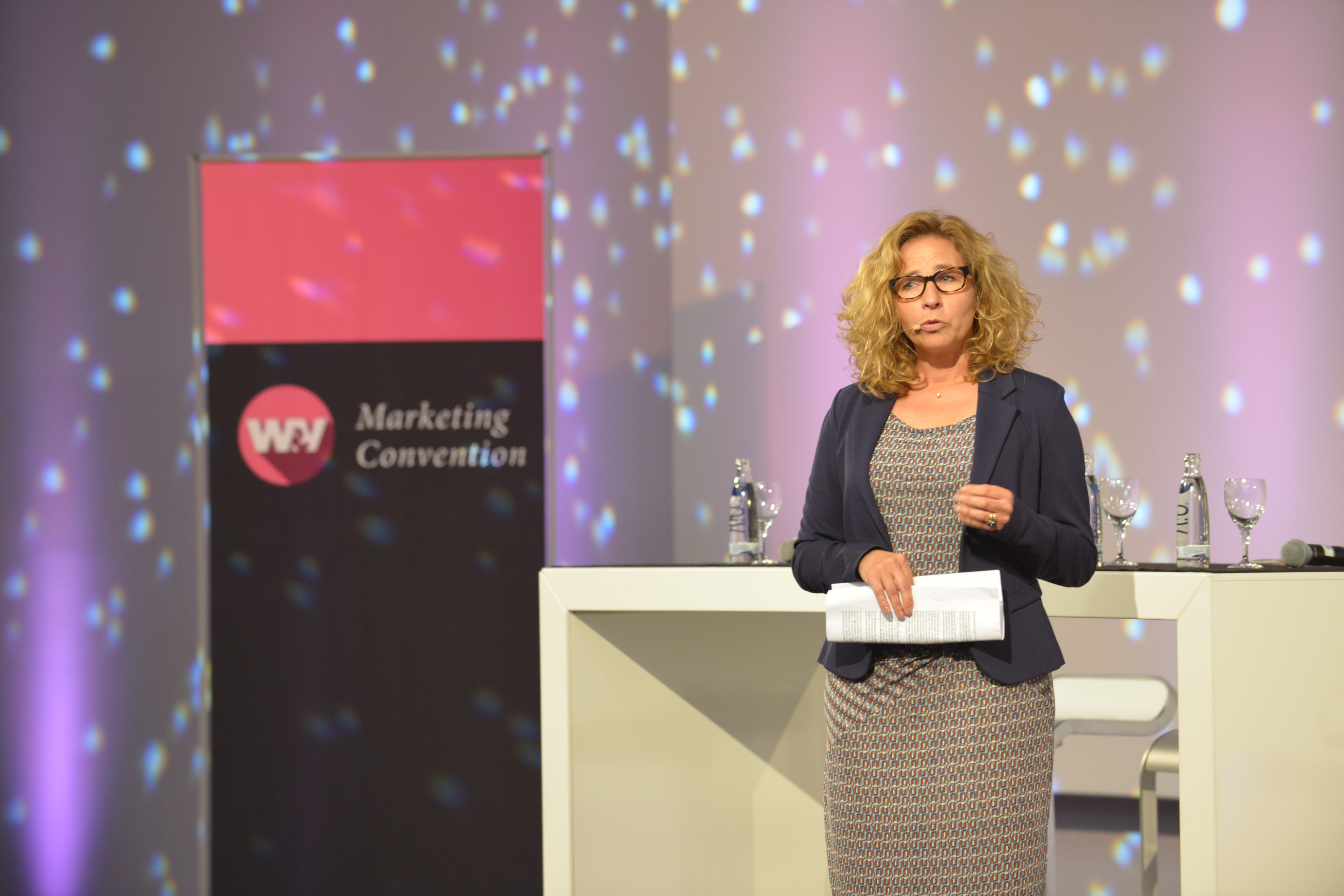 Referentin auf der Marketing Convention steht vor einem Roll-Up mit dem Logo der Veranstaltung.