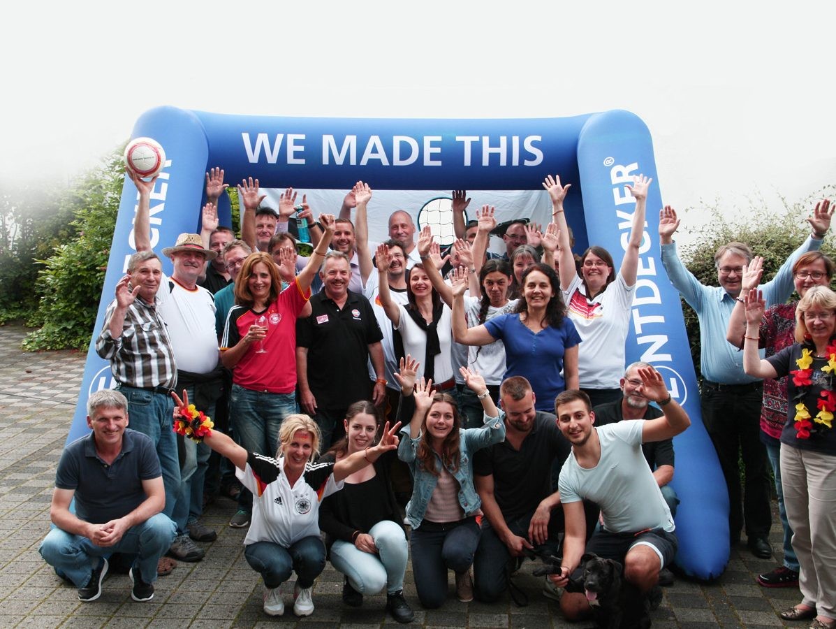 Gruppe von Menschen vor einer aufblasbaren Torwand mit dem Text 'WE MADE THIS'.