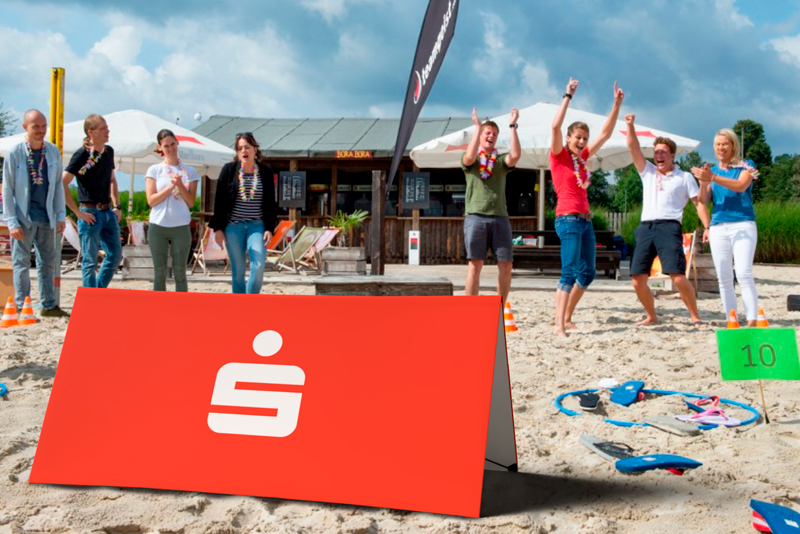 Werbebande Clickboard Strand mit dem Logo der Sparkasse, umgeben von Menschen, die am Strand feiern.