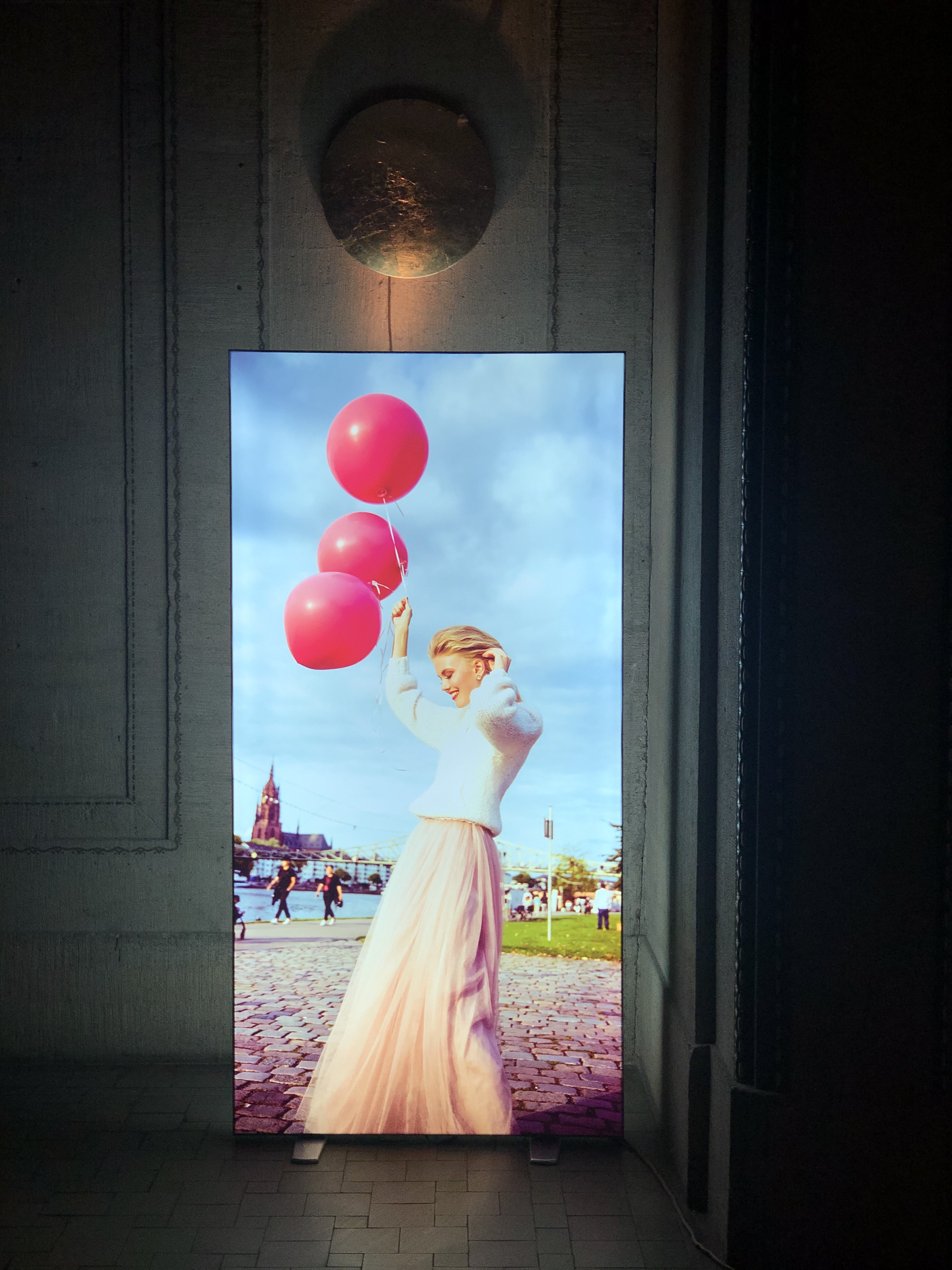 Leuchtender Pop Up LED Rahmen mit einer Frau, die in einem weißen Pullover und einem langen Rock steht und pinke Luftballons hält.