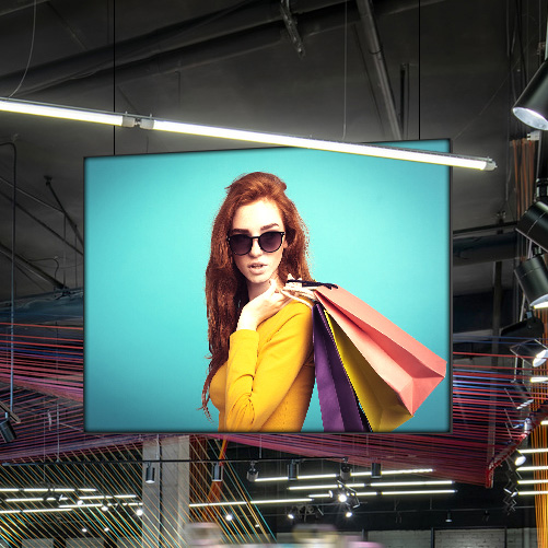 Deckenhänger Easyframe im Modegeschäft mit einer Frau in gelbem Oberteil und Sonnenbrille, die bunte Einkaufstaschen trägt.