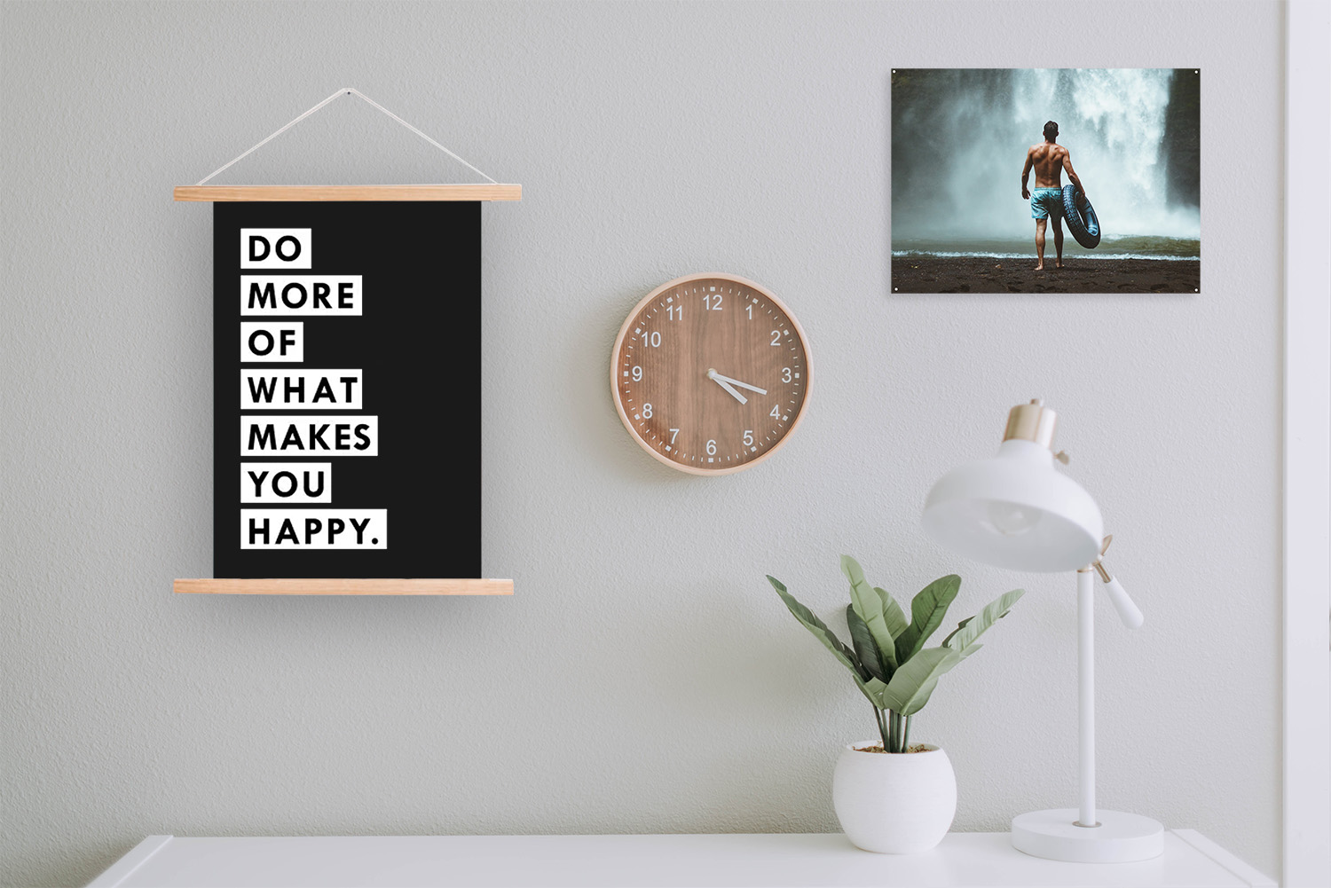Wanddeko mit dem Text 'DO MORE OF WHAT MAKES YOU HAPPY', eine Uhr, eine Lampe und eine Pflanze auf einem Tisch.