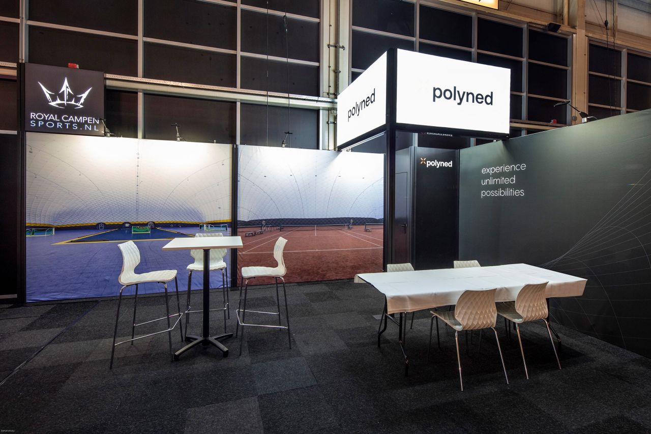Messestand von Royalsport mit dem Produktnamen 'polyned', zeigt Sportplatz im Hintergrund, Tische und Stühle im Vordergrund.