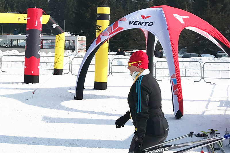 Person in Winterkleidung läuft an einem Vento Zelt vorbei, umgeben von Schnee und Sportequipment.