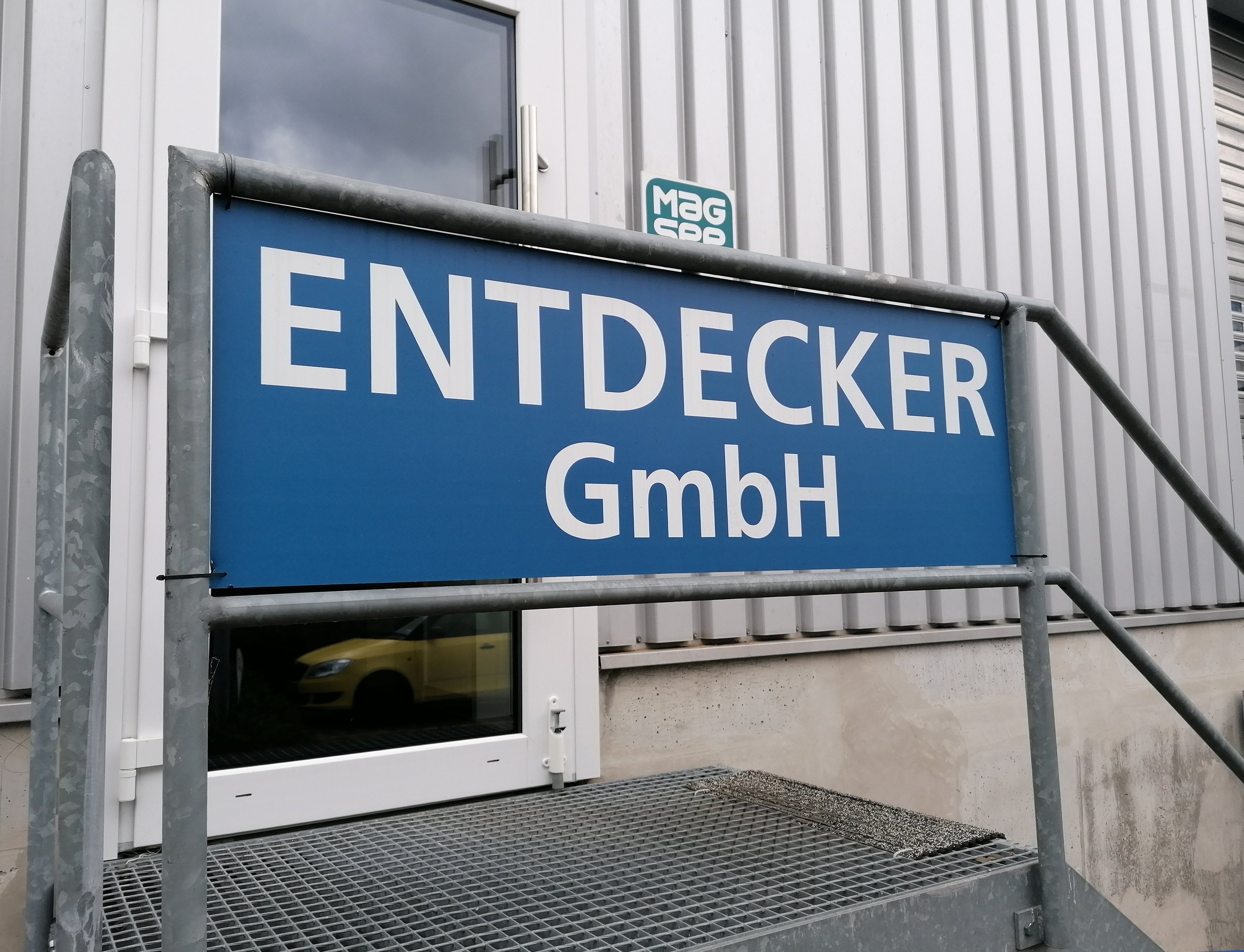 Eingangsschild der Entdecker GmbH mit blauem Hintergrund und weißer Schrift.