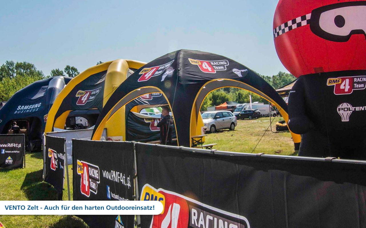 Aufblasbares Zelt von RMF Racing Team auf einem Outdoor-Event, mit verschiedenen Zelten und Fahrzeugen im Hintergrund.