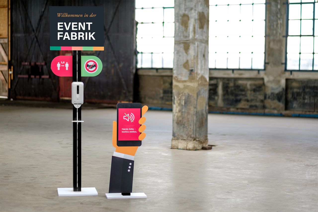 Desinfektionsständer mit Handdesinfektionsmittel und Smartphone-Symbol in einer Eventlocation.