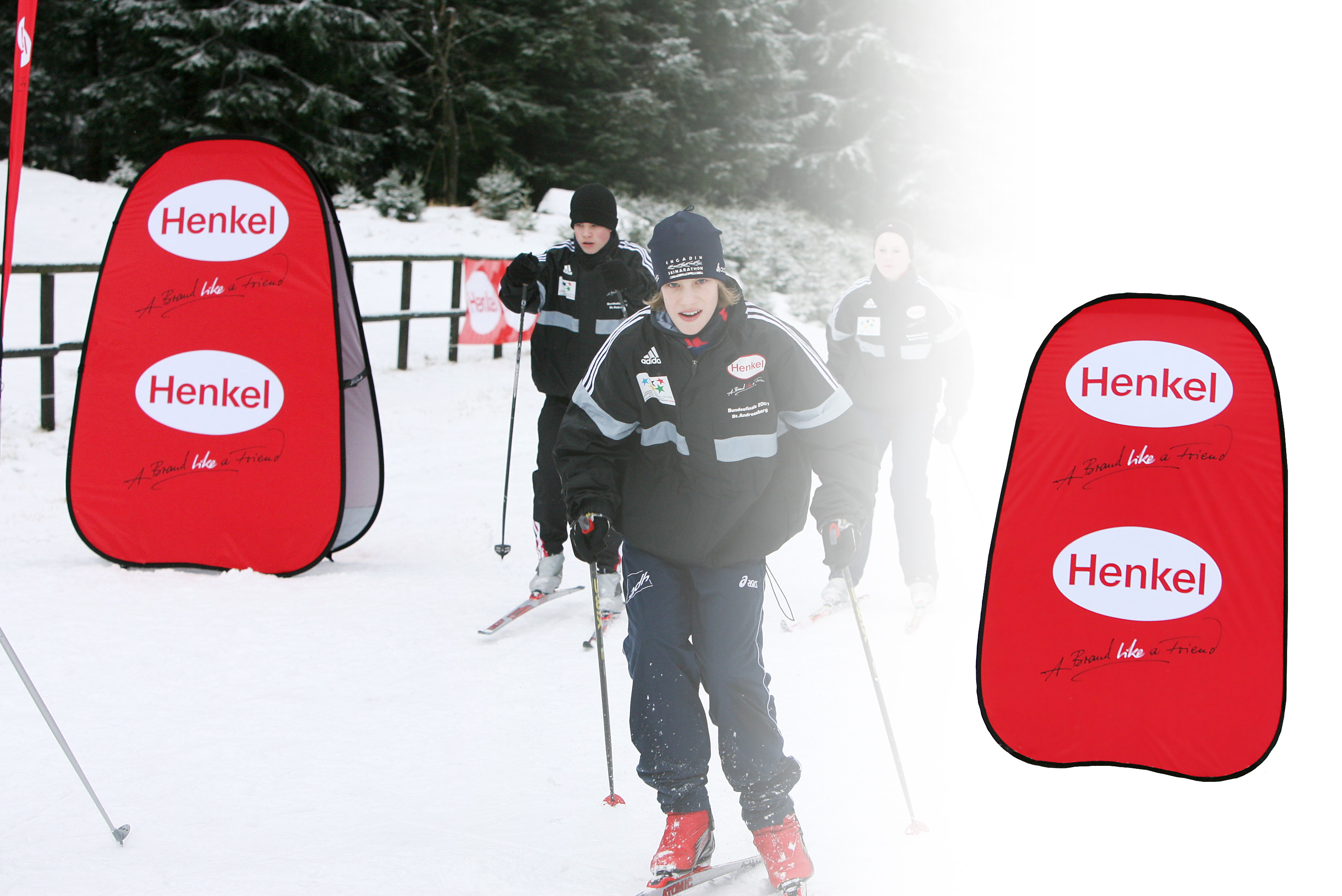 Werbebande Quickboard Vertikal von Henkel im Schnee mit Skifahrern im Hintergrund.