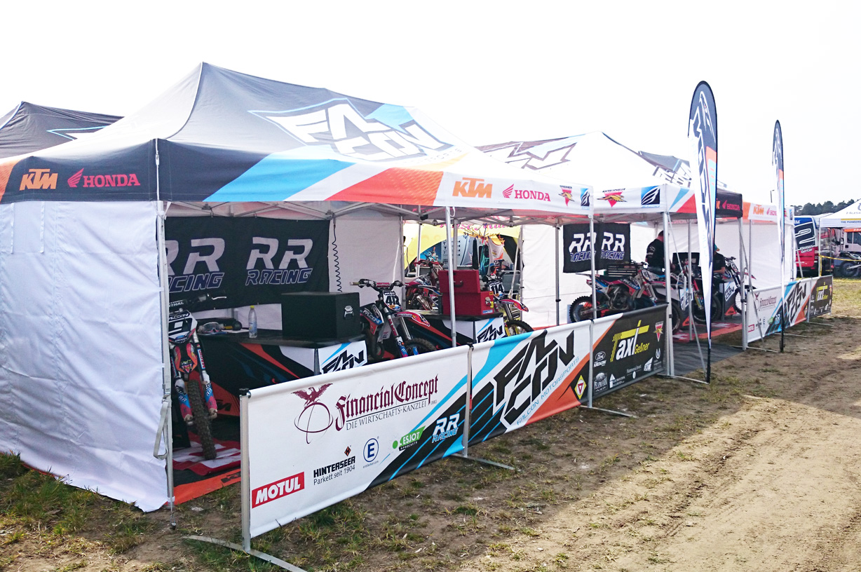 Zeltaufbau mit mehreren Faltzelten der Marke Falcon, die für ein Motorsport-Event genutzt werden. Sichtbare Motorräder und Sponsorenlogos.