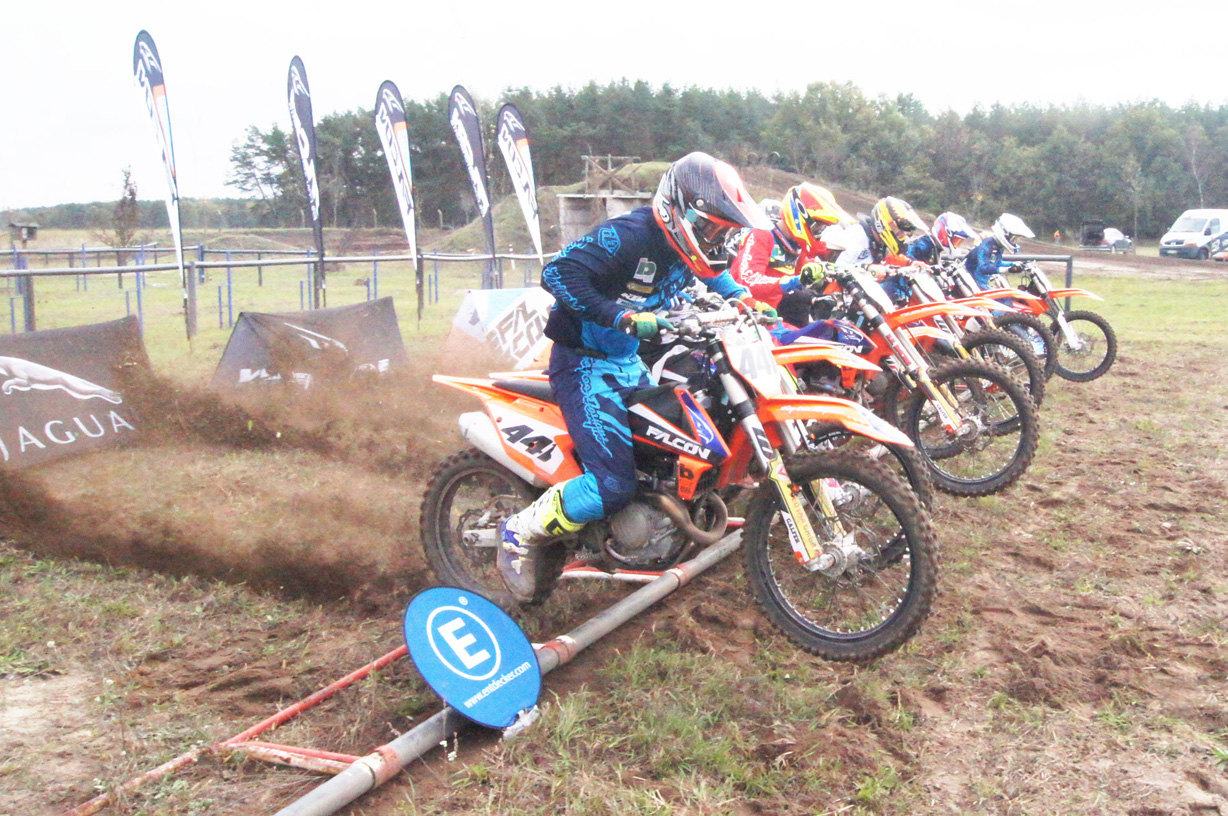 Motorradfahrer starten beim Rennen, im Vordergrund ein Fahrer auf KTM-Motorrad, im Hintergrund mehrere Beachflags von ENTDECKER.