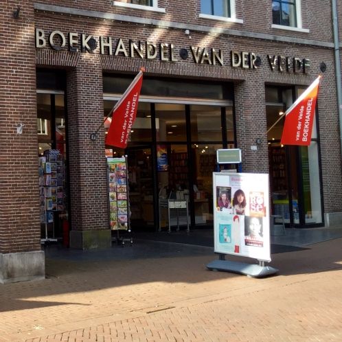 Kioskfahne vor der Buchhandlung Van der Velde, mit roten Fahnen und Werbetafeln.