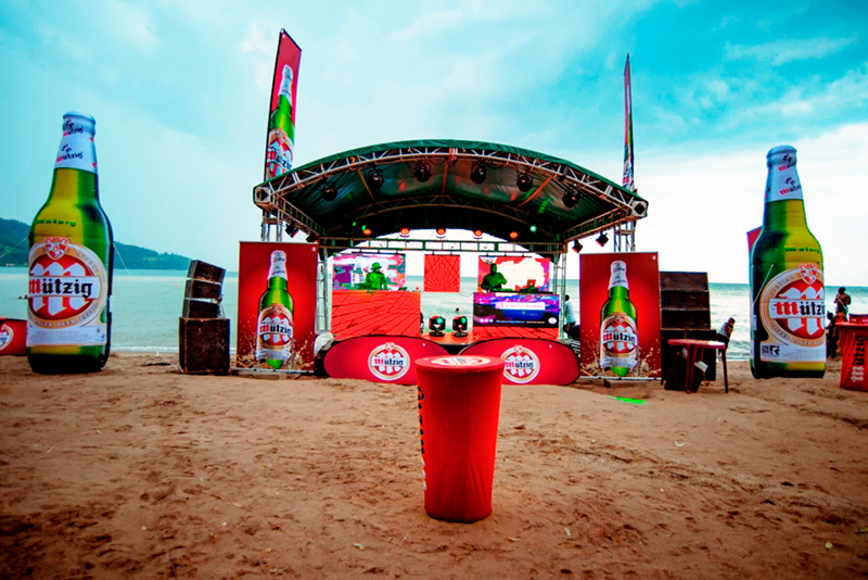 Bühne am Strand für das Event 'Beach Blow Up' mit großen Bierflaschen-Dekorationen und Lautsprechern.