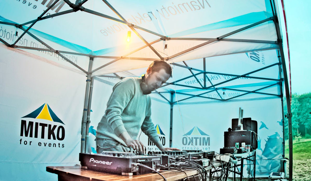 DJ steht an einem Mischpult unter einem Faltzelt mit dem Logo von MITKO bei einer Firmenfeier.