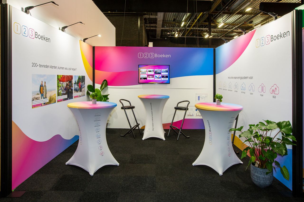 Messestand von 123Boeken mit buntem Hintergrund, Stehtischen und Bildschirm, der Informationen zeigt.