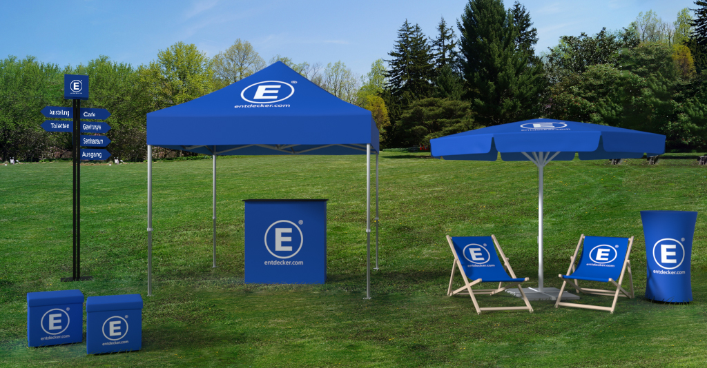 Messeoutdoor-Produkt von ENTDECKER: blauer Pavillon, Sonnenschirm, Liegestühle und Werbebanner auf einer Wiese.