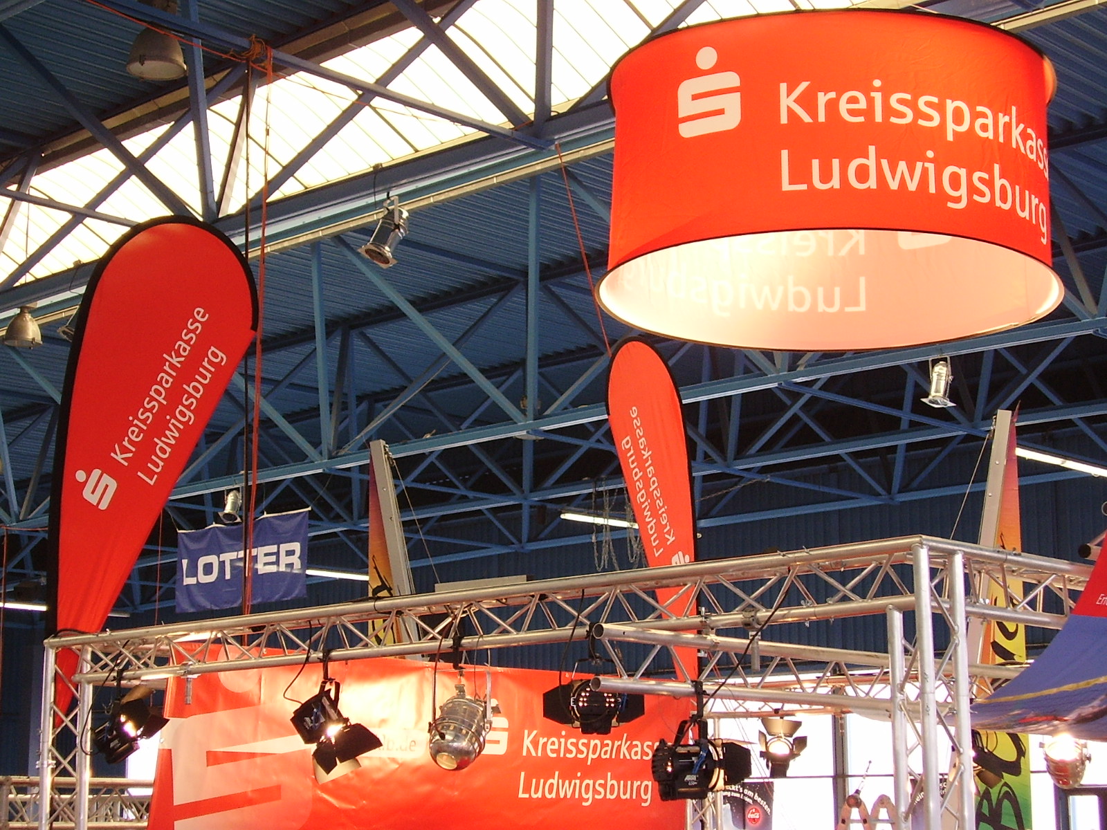 Runde Deckenhänger mit dem Toyota-Logo über einem Messestand, Besucher interagieren mit einem Rennwagen.