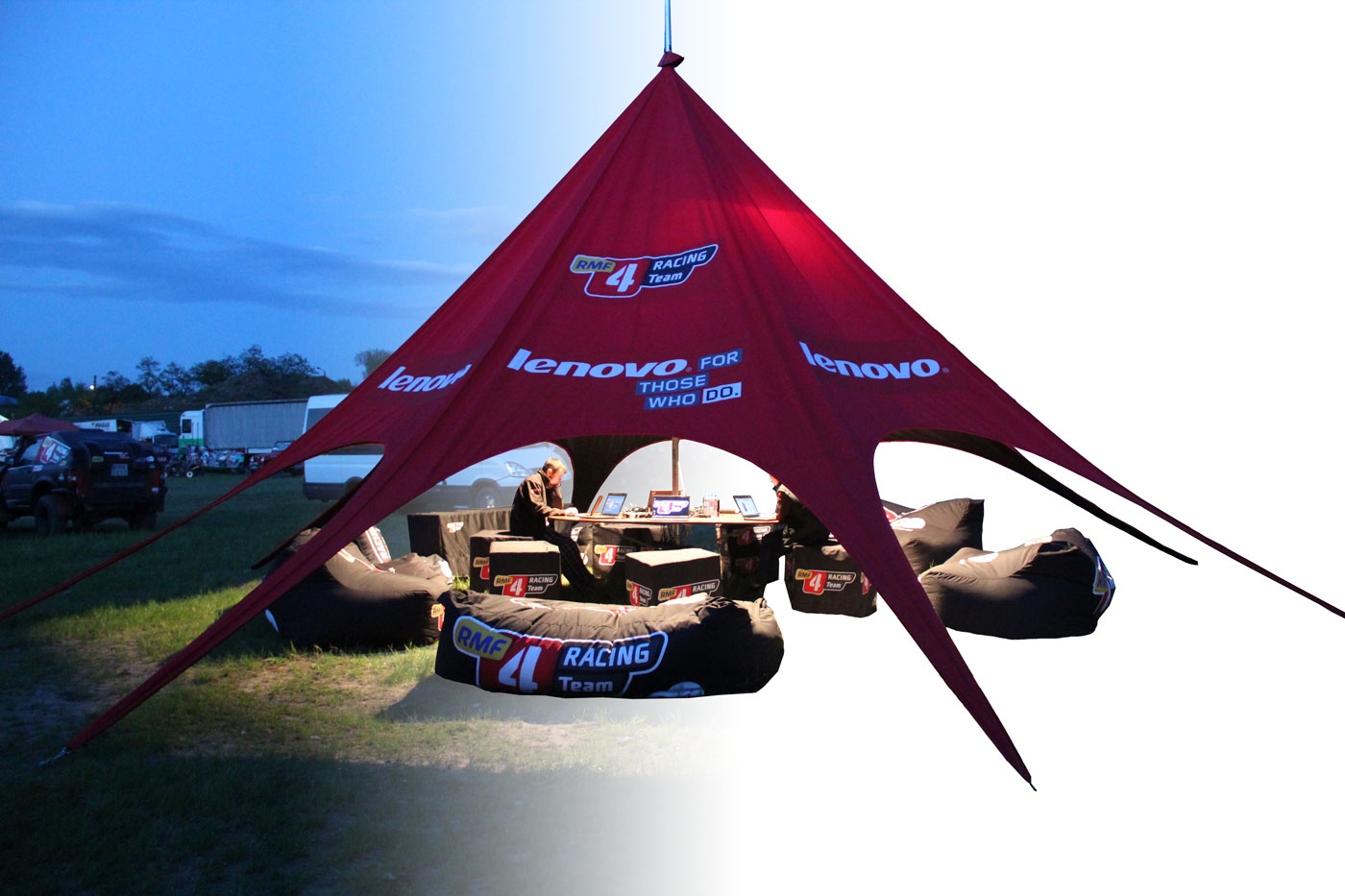 Beleuchtetes Sternzelt von Lenovo Racing bei Nacht, mit Sitzgelegenheiten und Tisch im Inneren.