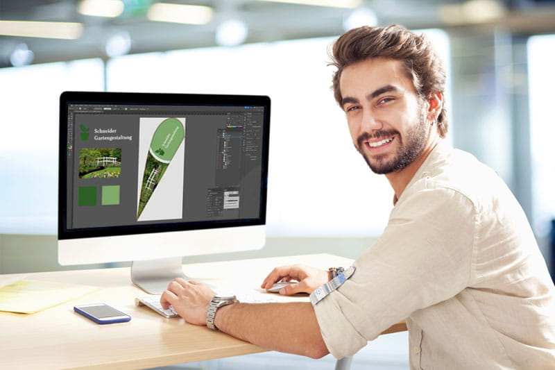 Ein junger Mann sitzt an einem Computer und arbeitet an einem Layout für den Produkt 'Unser Layoutservice'.