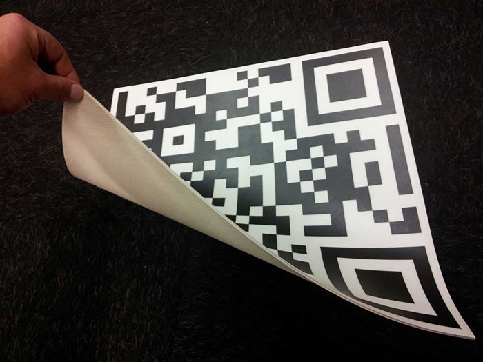 Fußbodenbelag mit QR-Code-Motiv, teilweise umgeklappt, zeigt den QR-Code und die Unterseite des Belags.