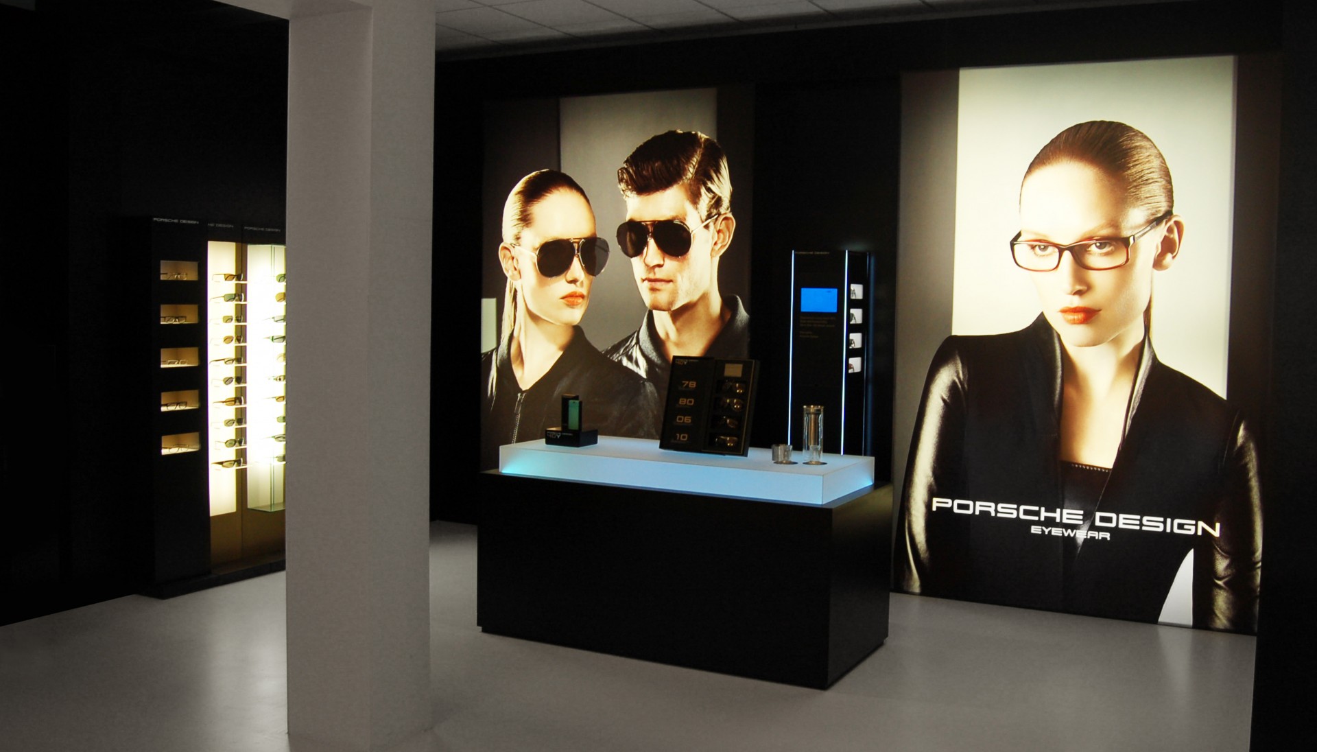 Messewand mit zwei großen Bildern von Modellen in Sonnenbrillen, im Hintergrund ein eleganter Verkaufsbereich für Porsche Design Eyewear.