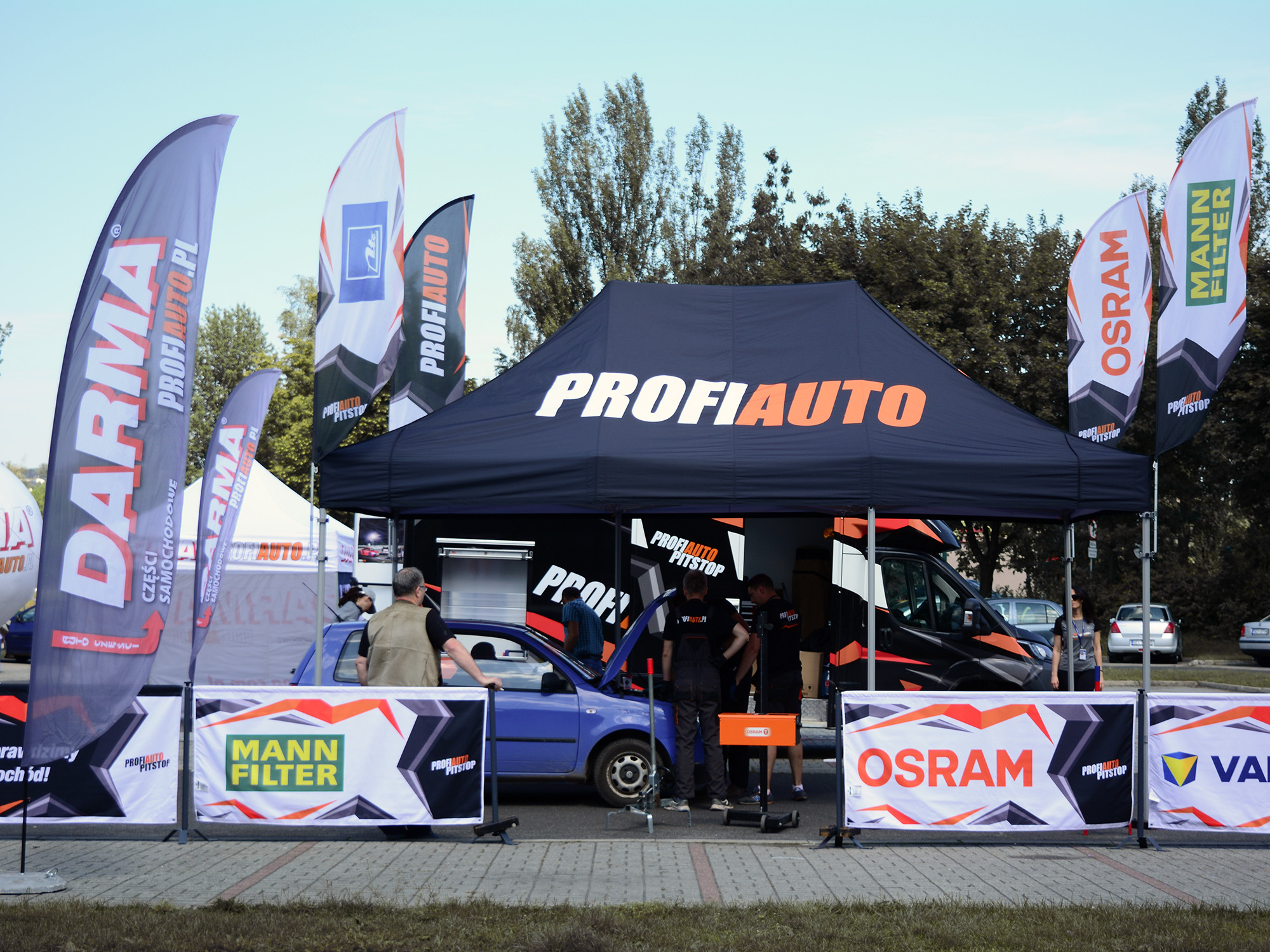 Zelt mit der Aufschrift 'PROFIAUTO' auf einem Event, umgeben von Werbefahnen für Marken wie DARMA, MANN FILTER und OSRAM.