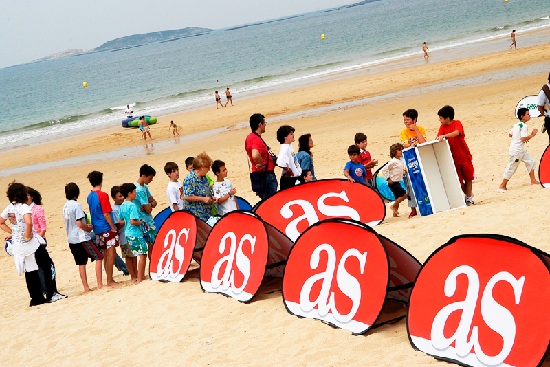 Werbebande Quickboard Strand mit dem Logo 'as' am Strand, umgeben von Kindern und einem Kiosk.